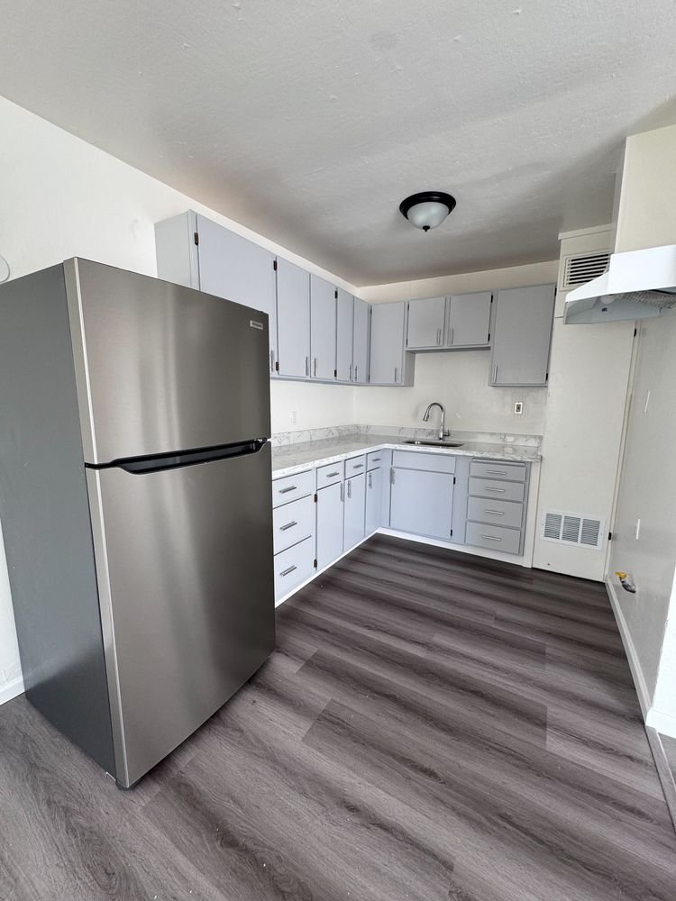 Renovated kitchen with gray shaker cabinets, stainless refrigerator and plank flooring